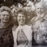 A black and white photograph shows a young woman with her parents on either side of her.
