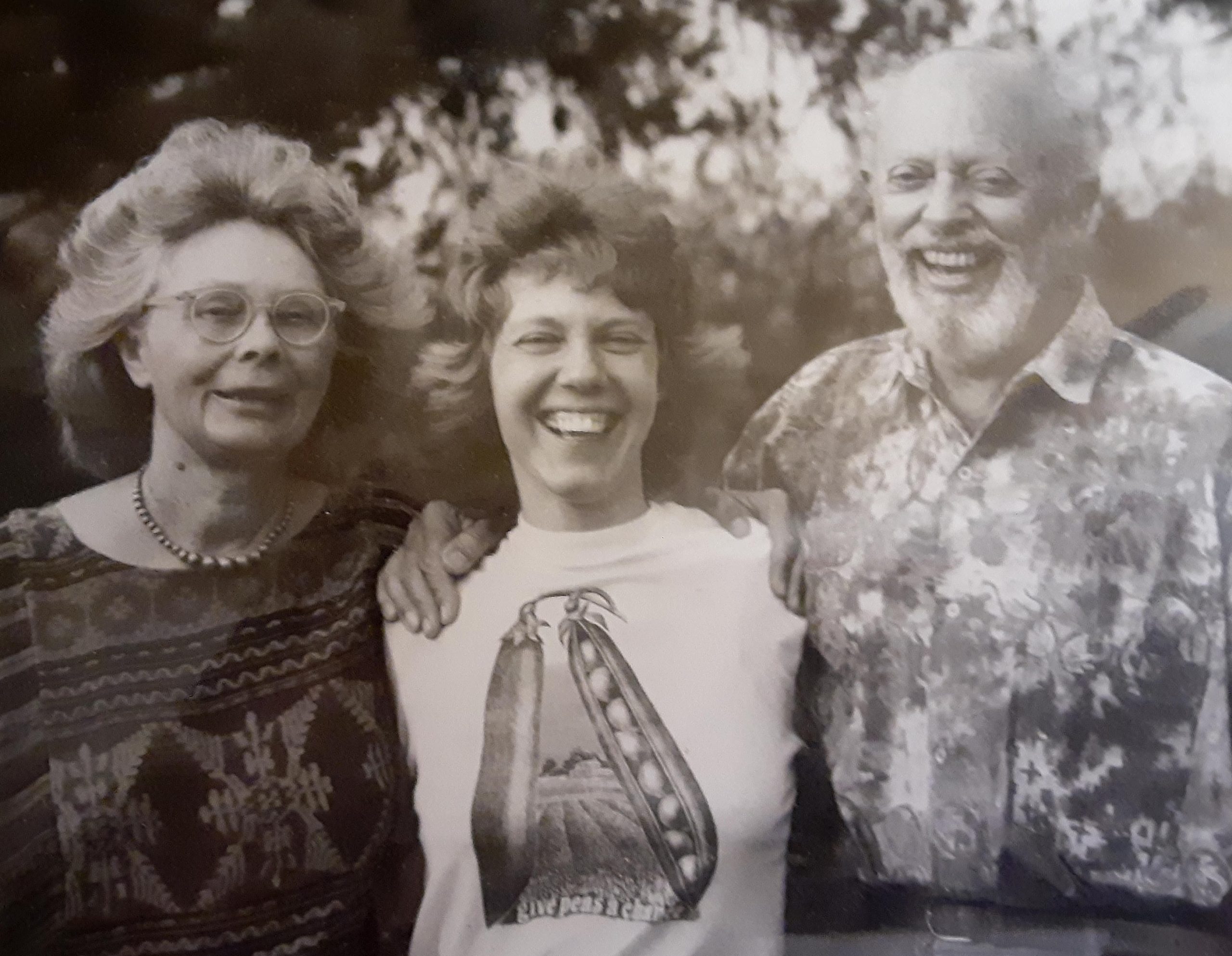 A black and white photograph shows a young woman with her parents on either side of her.