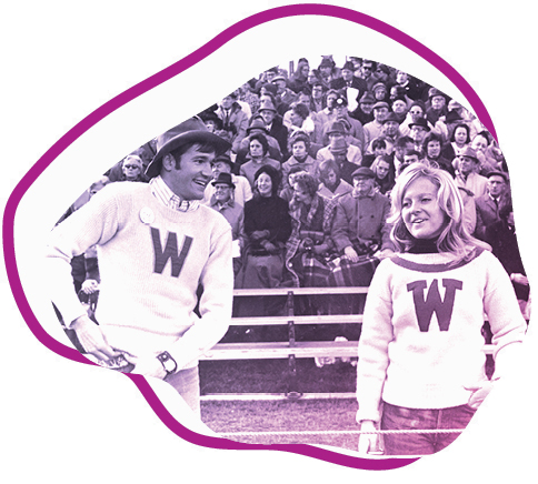 men and woman in wearing W sweaters in front of large crowd on bleachers
