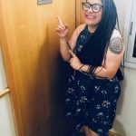person standing by a door smiling and pointing to sign on it that reads F303