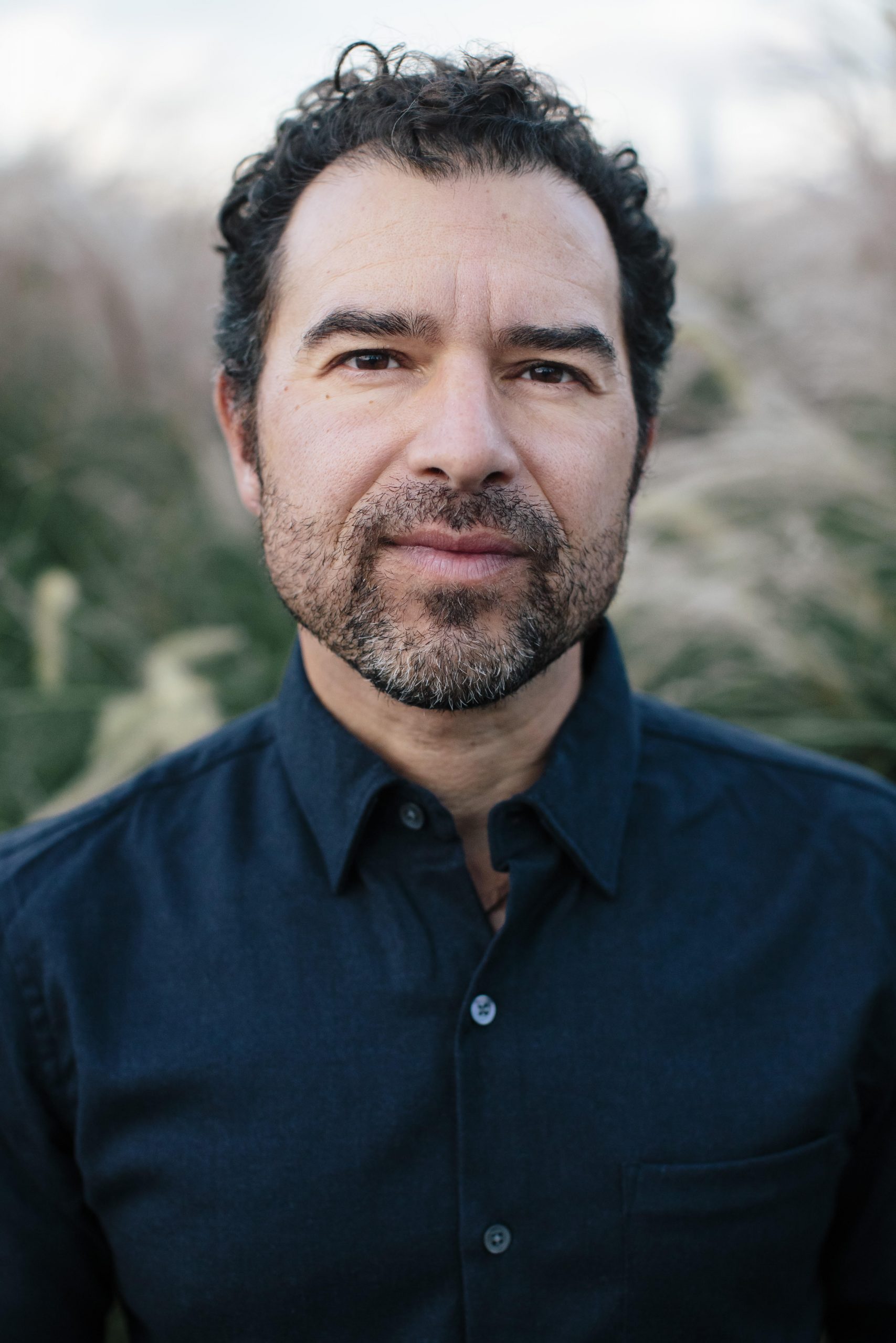 photo of a man wearing a dark blue shirt with curly hair and a beard.
