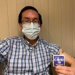 a person sitting down wearing a face mask and holding a sticker that reads 