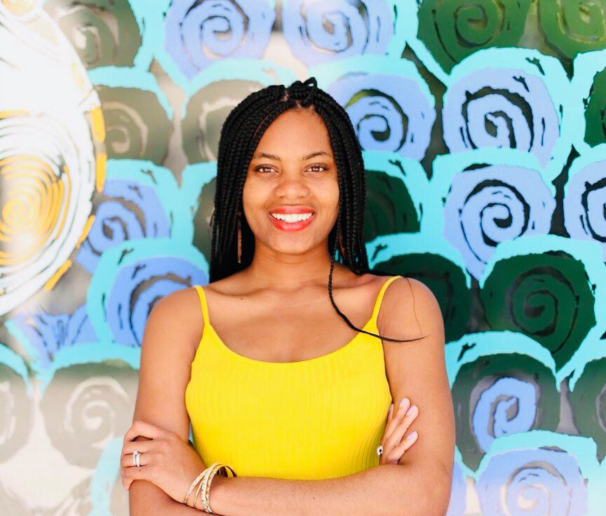 a person wearing a yellow top with long braided hair and a background with abstract circular green and aqua blue patterns