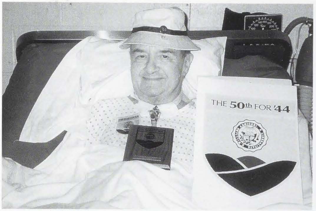 Man in hat propped up in bed with 50th Reunion paraphernalia on his chest