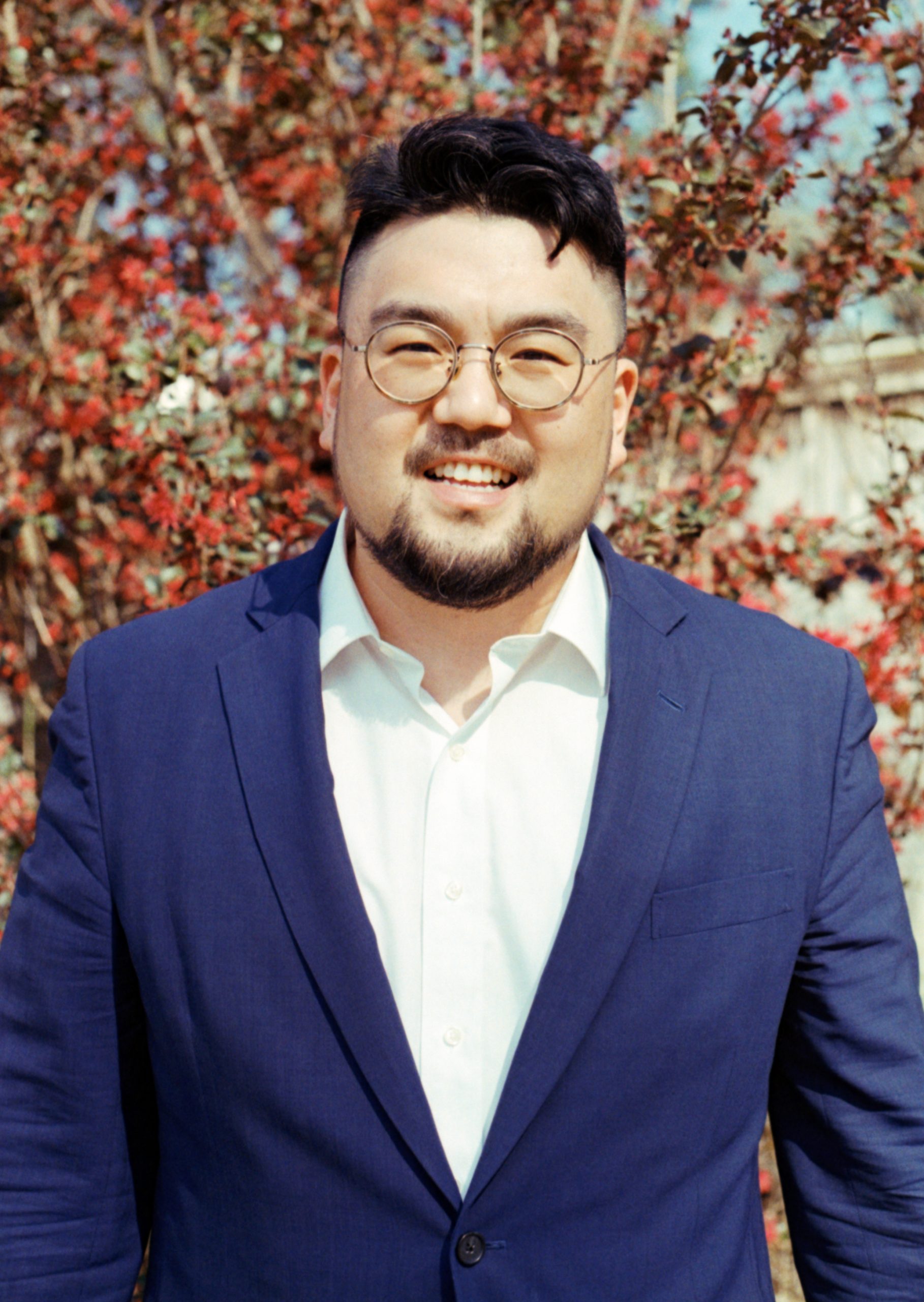 person wearing glasses, with a blue suit jacket and white shirt underneath