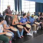 A row of people drumming in front of a mirrored wall
