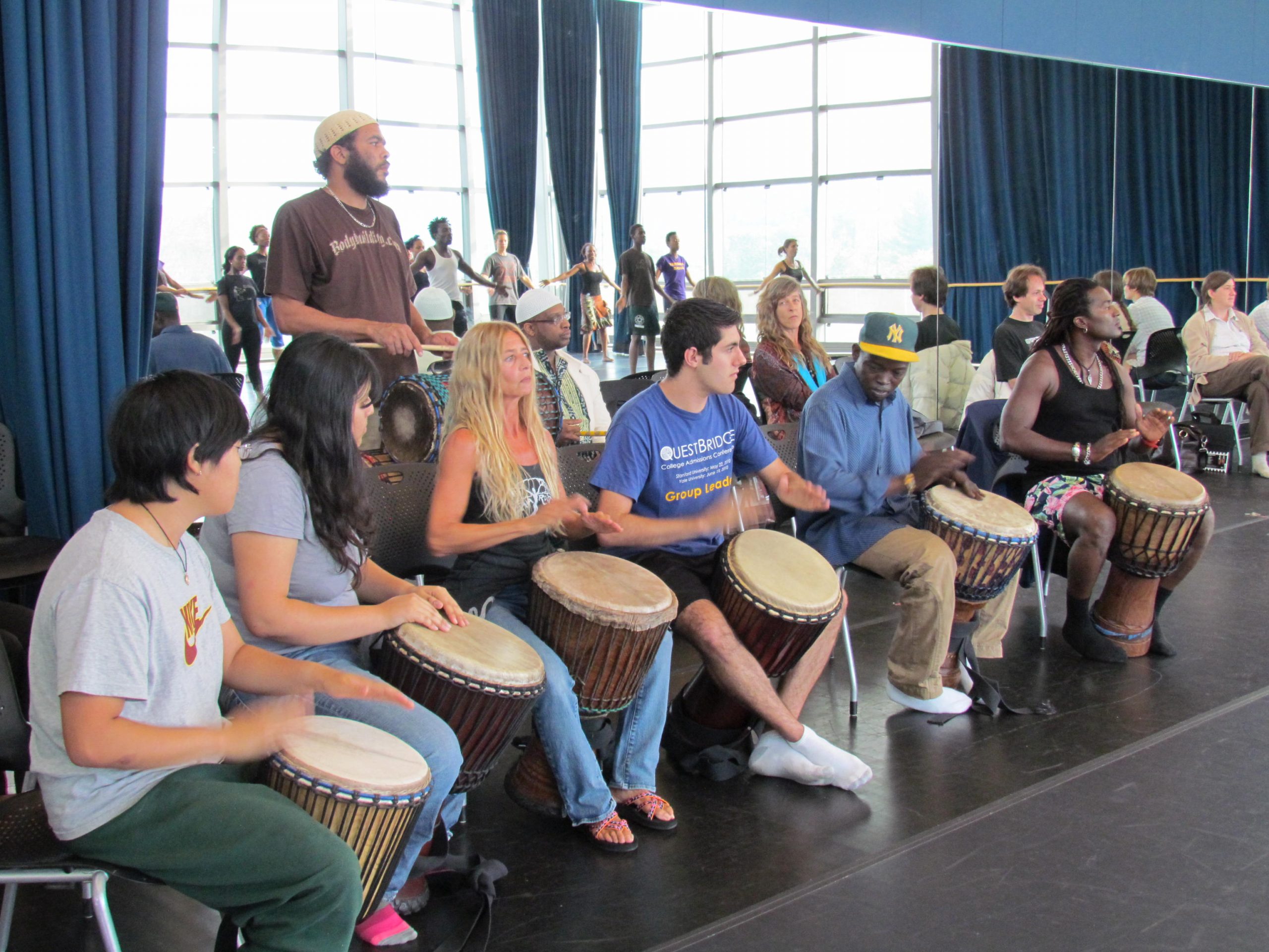 A row of people drumming in front of a mirrored wall
