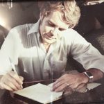 Man leaning over writing page with pen in hand