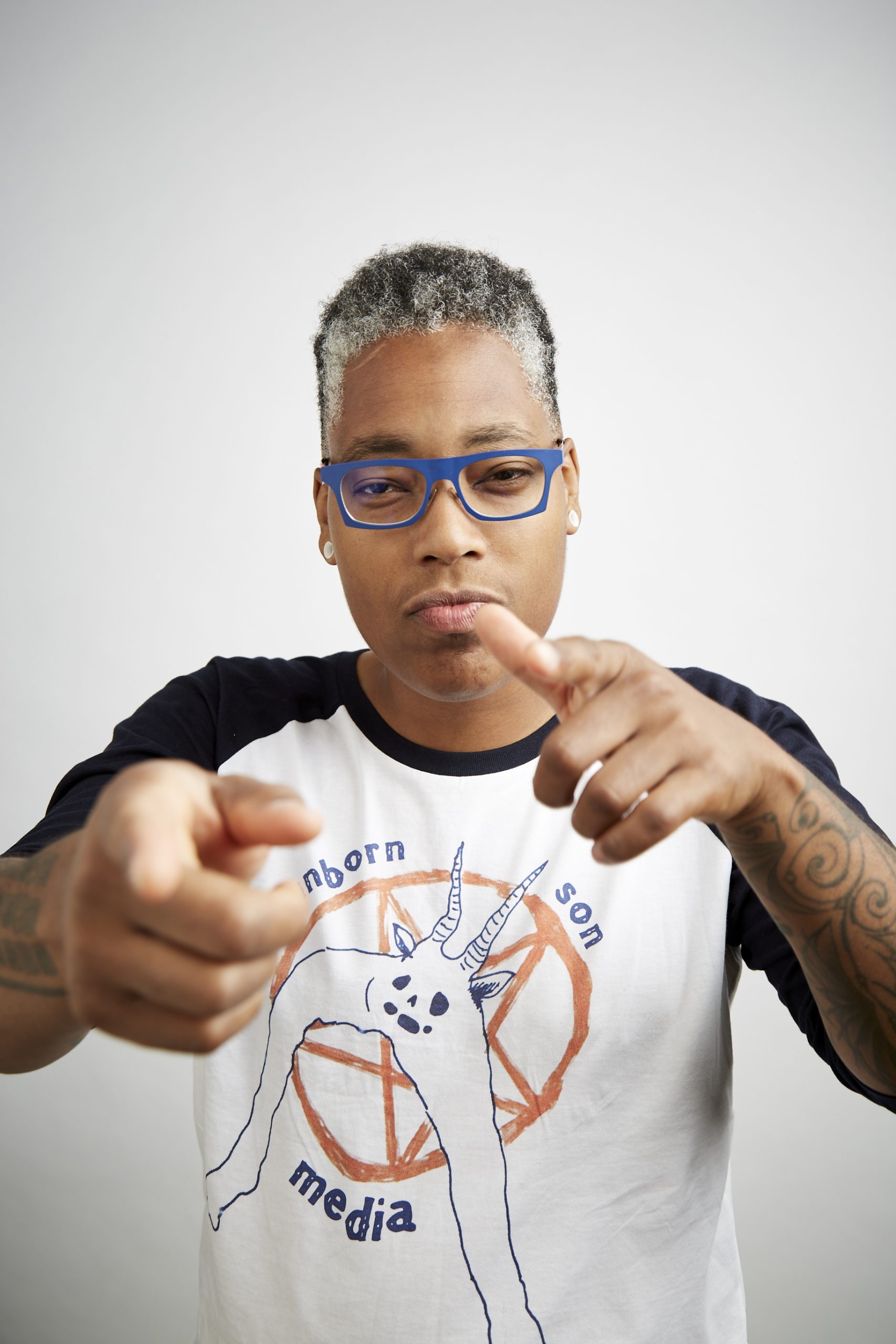 saifa flex and pointing straight ahead, wearing glasses and a shirt with words that say 'unborn, son, media.'