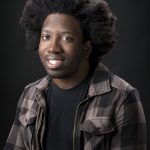 profile photo of a person smiling, wearing a black and gray square jacket with black t-shirt underneath, and a black background