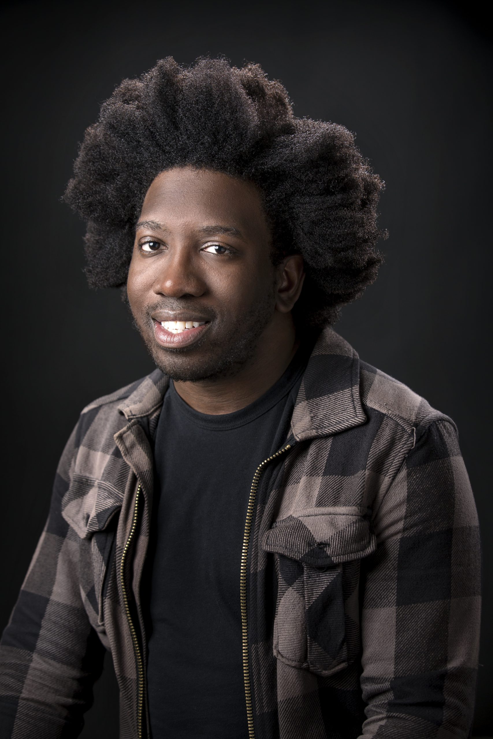 profile photo of a person smiling, wearing a black and gray square jacket with black t-shirt underneath, and a black background