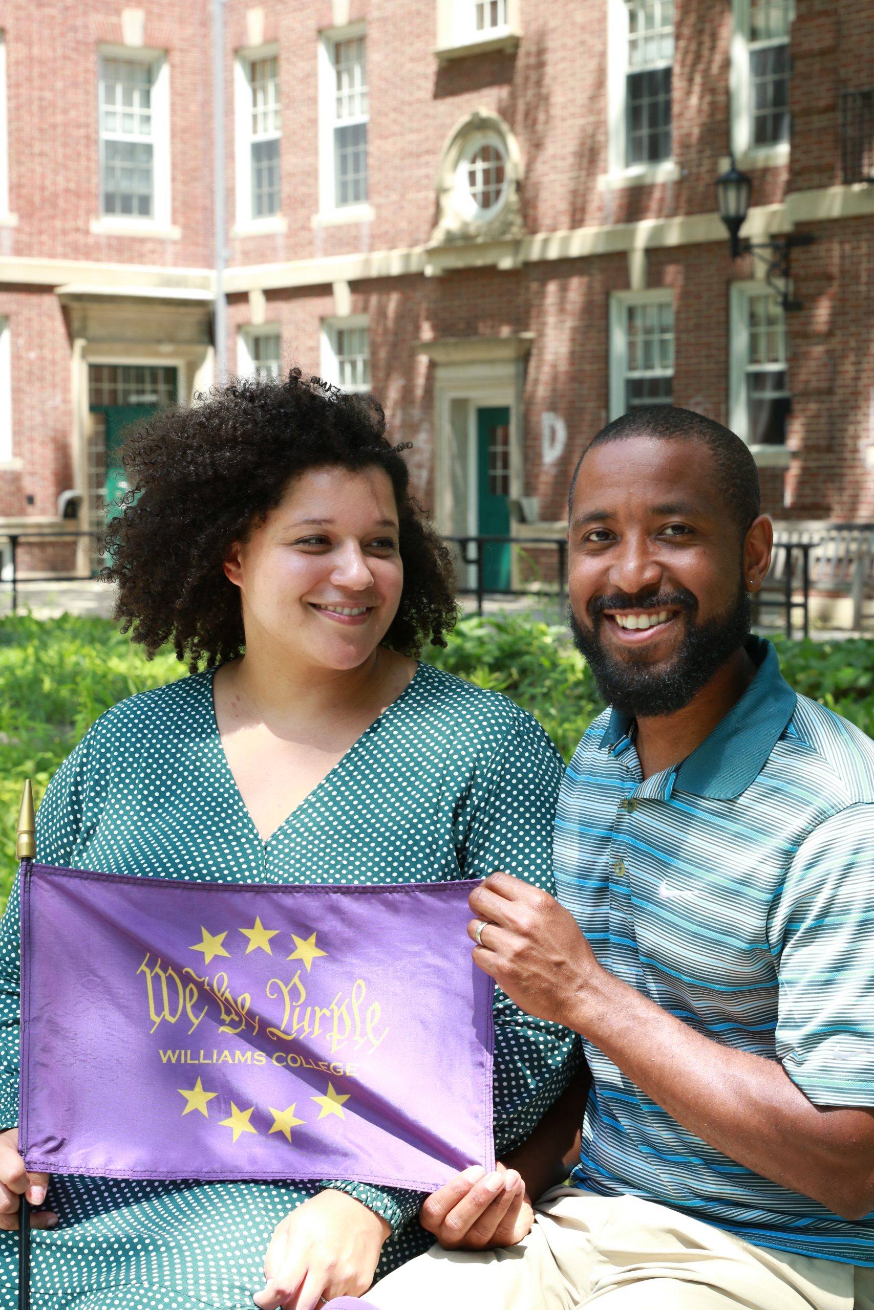 Twink and Markus holding 'We the Purple' flag while sitting in front of Williams Hall.