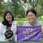 Caroline, Kevin, and Pixie holding a We the Purple flag while sitting down at a park table.