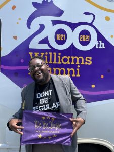 Eze holding a 'We the Purple' flag in front of the RV.