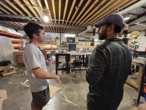 2 people in conversation side a van building shop