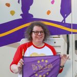 a woman holding a purple flag that says 'We the Purple' with a backdrop of graphics with cows dancing