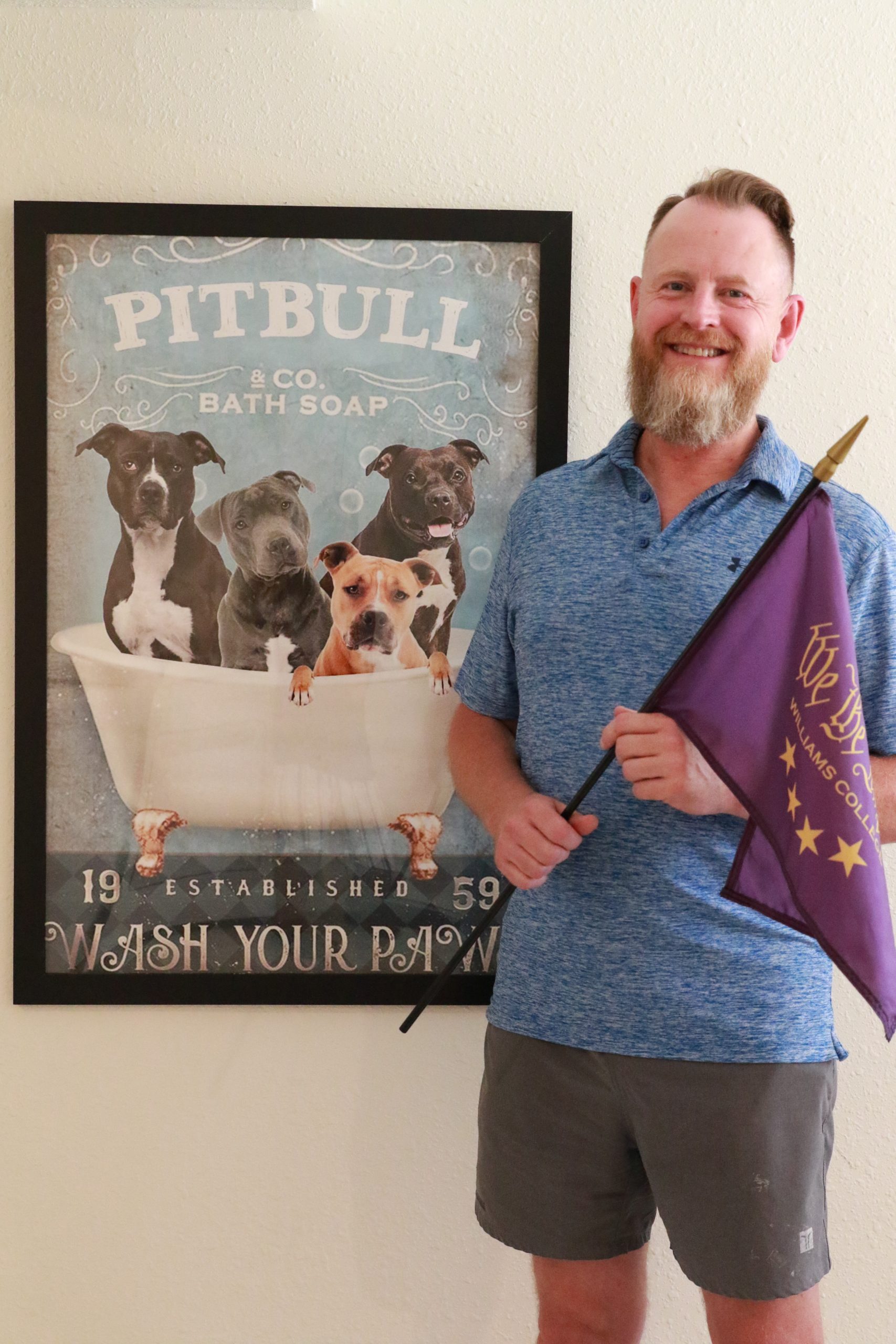 person standing next to a poster depicting a group of 4 pitbulls inside a bathtub with text that reads ' Pitbull and Co Bath Soap - Wash your Paw'