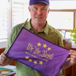 a man wearing a green shirt and holding a purple flag that says 'We the Purple, Williams College,