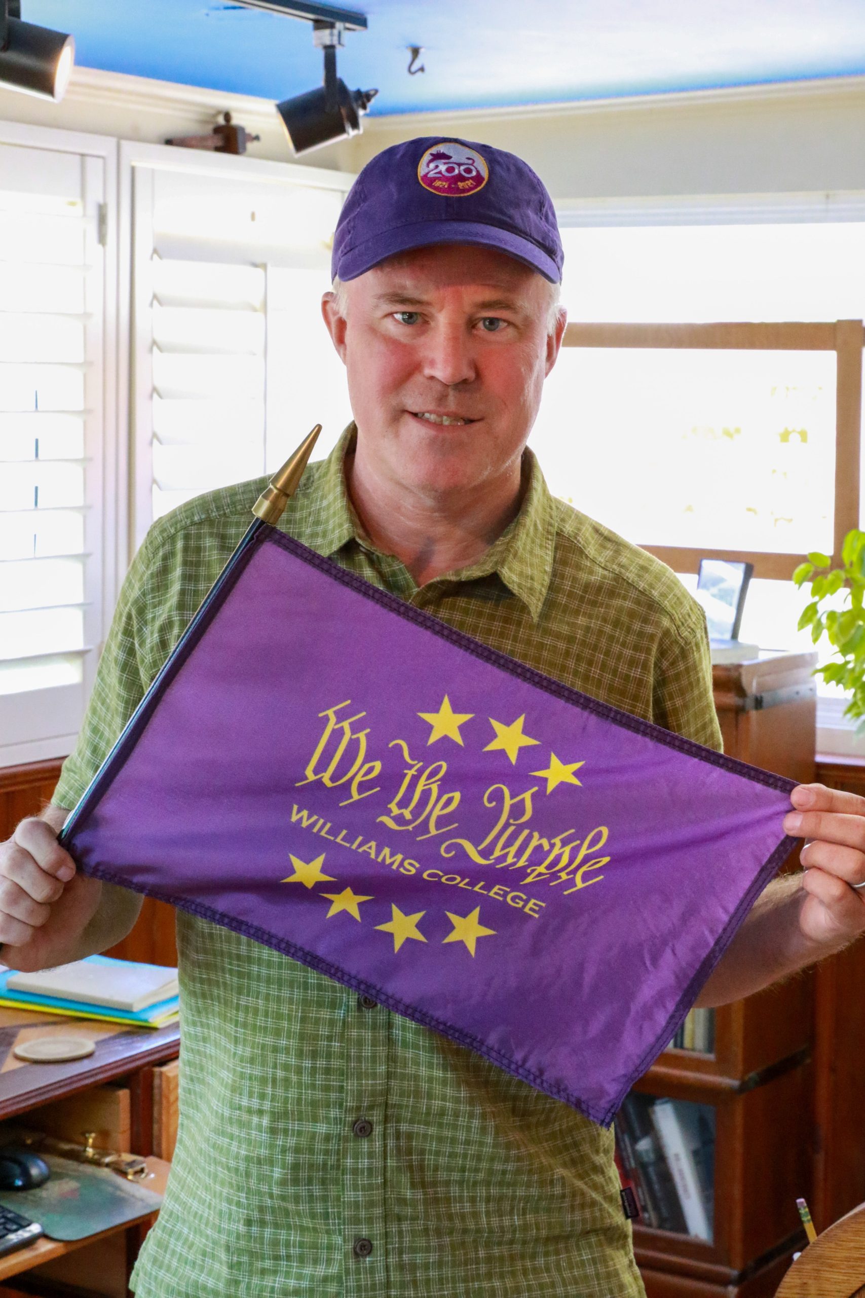a man wearing a green shirt and holding a purple flag that says 'We the Purple, Williams College,