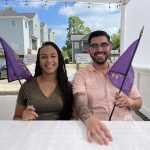 2 people sitting down at a table holding down purple flags
