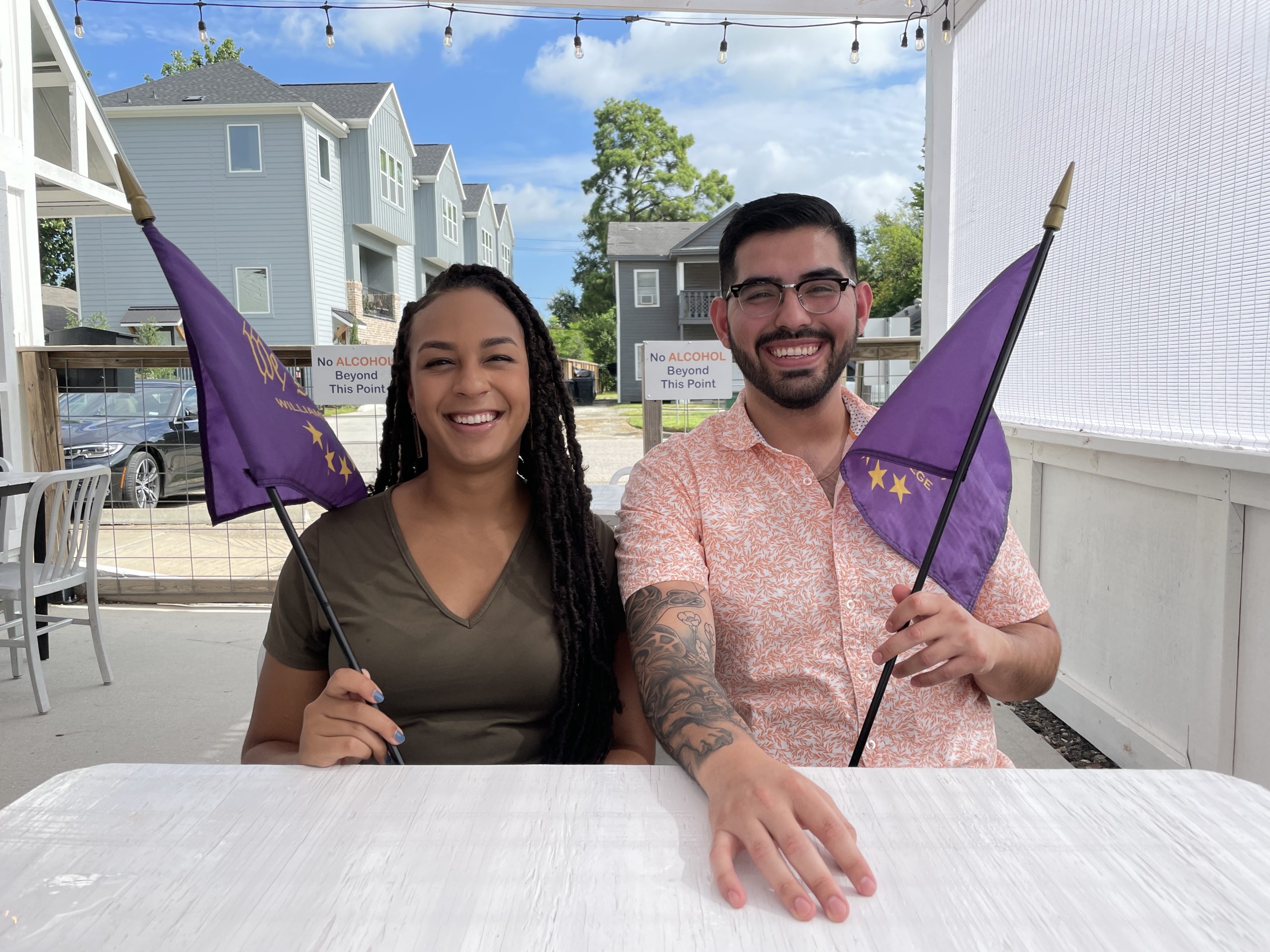 2 people sitting down at a table holding down purple flags