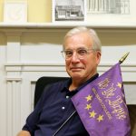 a man holding a purple flag while sitting down