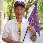 a person wearing a white shirt and a purple baseball cap while holding a purple flag