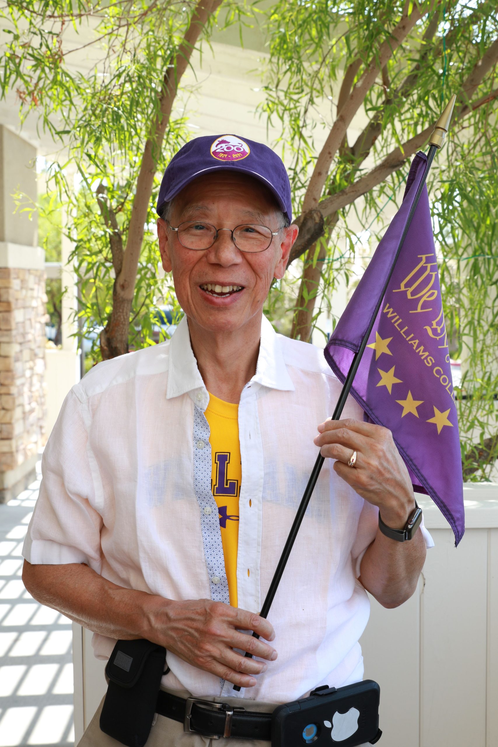 a person wearing a white shirt and a purple baseball cap while holding a purple flag