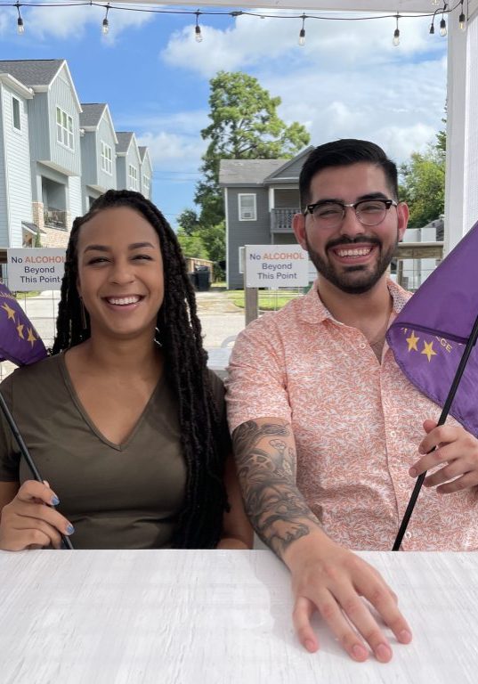 2 people sitting down at a table holding down purple flags
